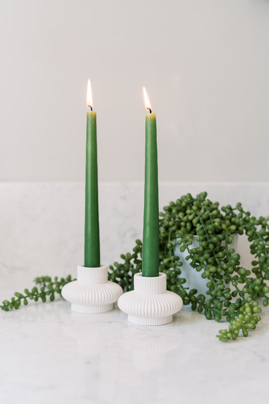 White concrete lantern shaped taper candle holders on marble surface with green candles.